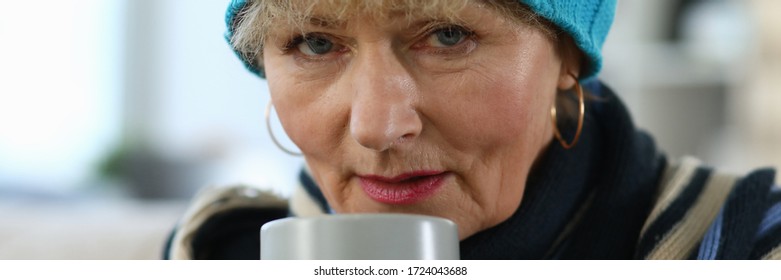 Elderly woman feels sick and drinks tea at home. Lady in knitted hat takes cup tea. Parents do not tolerate loneliness, suffer from complications. Chronic diseases, frequent concomitant aging - Shutterstock ID 1724043688