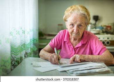 An elderly woman fills in utility bills.