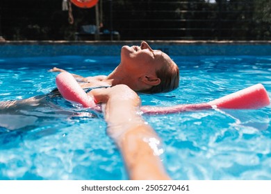 An elderly woman floats calmly in a swimming pool with her eyes closed, enjoying the relaxation of the water on a bright sunny day - Powered by Shutterstock