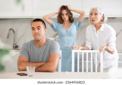 Elderly woman gets angry during quarrel with man and woman couple in kitchen - Powered by Shutterstock