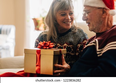 Elderly woman giving a gift to her husband for christmas. Senior couple exchanging gifts celebrating christmas at home. - Powered by Shutterstock