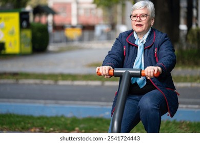 An elderly woman with glasses and gray hair engages in fitness training on outdoor exercise equipment in an urban park during autumn. Dressed in comfortable clothes, she is committed to her health - Powered by Shutterstock