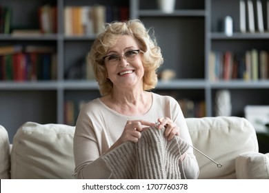 Elderly woman in glasses sit on couch at home smile look at camera holding knitting needles and yarn knits clothes for loved ones, favorite activity and pastime, retired tranquil carefree life concept - Shutterstock ID 1707760378