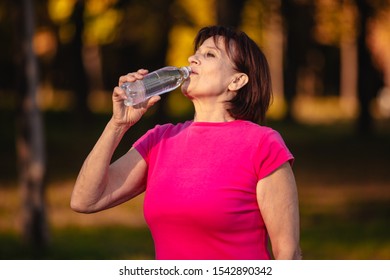 Elderly Woman Goes In For Sports. Drinking Water From A Bottle At Sunset