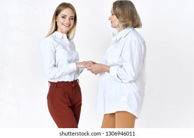 An elderly woman and granddaughter in white shirts are standing side by side on a light background - Shutterstock ID 1306946011
