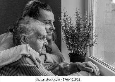 An elderly woman, a grandmother looks out the window, a granddaughter approaches her and hugs, a happy family - Powered by Shutterstock