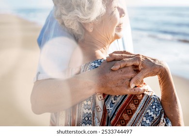 Elderly woman with gray hair embraces by her husband on a sunny beach. Close-up of hands, patterned shawl, and ocean in the background. Senior couple embrace on summer holiday at the beach. - Powered by Shutterstock