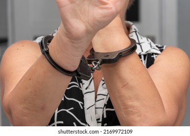 An Elderly Woman In Handcuffs Hides Her Face On A Blurry Background. Elderly Criminal, Criminal Liability Of Pensioners, Domestic Violence Against Women.