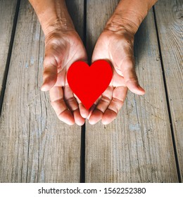 Elderly Woman Hands Closeup Holding Red Heart. Rustic Wooden Table Background. Love, Warmth, Take Care Concept, Valentines, Mothers Day, Donate, Help.