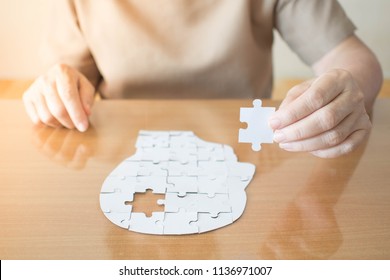 Elderly woman hands holding missing white jigsaw puzzle piece down into the place as a human head brain shape. Creative idea for memory loss, dementia, Alzheimer's disease and mental health concept. - Shutterstock ID 1136971007