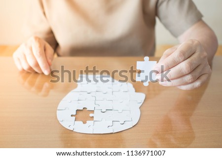 Elderly woman hands holding missing white jigsaw puzzle piece down into the place as a human head brain shape. Creative idea for memory loss, dementia, Alzheimer's disease and mental health concept. Foto stock © 