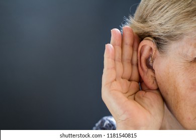 Elderly Woman With Hearing Aid On Grey Background. Close Up. Defect And Hearing Loss Concept.