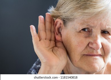Elderly Woman With Hearing Aid On Grey Background. Age-related Hearing Loss, Symptoms And Treatment Concept.