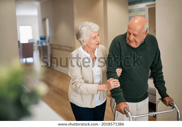 Elderly woman help\
her husband walking using walker in nursing home. Senior woman\
helping disabled man with walking frame. Lovely wife holding hands\
of old husband in care\
centre.