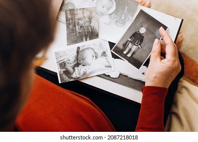 An elderly woman holding album with black and white retro photographs of childhood, remembering herself as little girl, child. Happy memories, nostalgia concept. Selective focus on vintage, old images - Shutterstock ID 2087218018