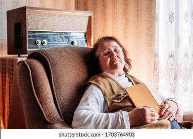 Elderly woman holding a book, napping in the chair by the window. Old, retro radio behind her. Afternoon light - Powered by Shutterstock