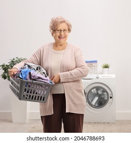 Elderly Woman Holding A Laundry Basket With Clothes Inside A Bathroom