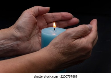 An Elderly Woman Holds A Burning Candle In Her Hands, Selective Focus. Concept: Turning Off Heating And Electricity, Reducing Room Temperature, It's Cold In The Apartment.