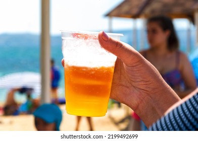 An Elderly Woman Holds A Glass Of Beer In Her Hand While Relaxing On The Beach. Sunny Day, Summer.