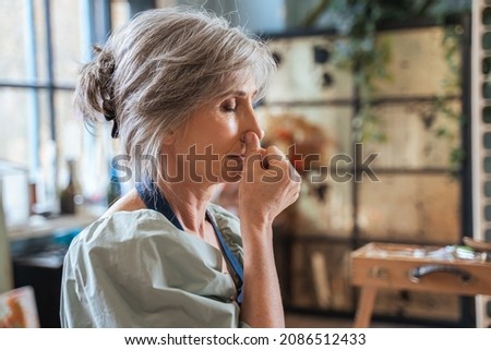 Elderly woman keeping her eyes closed and doing breathing exercise while closes nostril