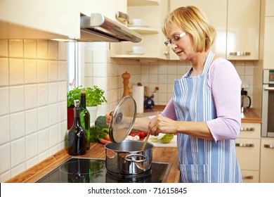 Elderly Woman In Kitchen On A Stove Cooking Soup