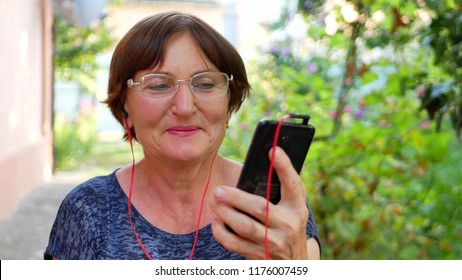 Elderly Woman Listen Music By Red Headphones And Black Smartphone