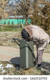 An Elderly Woman Is Looking For Food In A Trash Can.