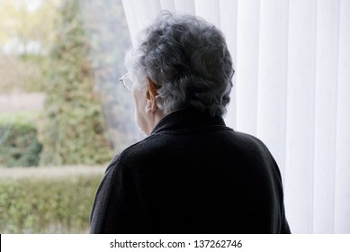 Elderly Woman Looks Out Of Her Window