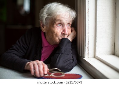An elderly woman looks sadly out the window. - Shutterstock ID 521175373