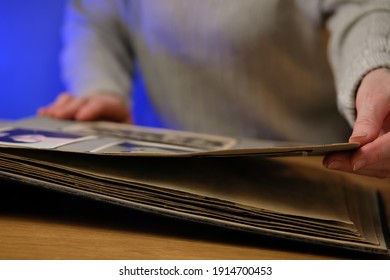 Elderly Woman Looks Through An Family Album With Old Photos At Table At Home. Old Granny Memories Past Times And Remembering His Life.