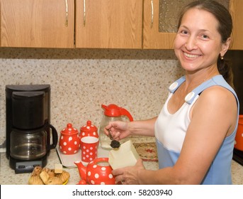 Elderly Woman Making Tea  In Red Teapot At Kitchen