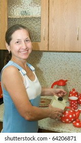 Elderly Woman Making Tea  In Red Teapot At Kitchen