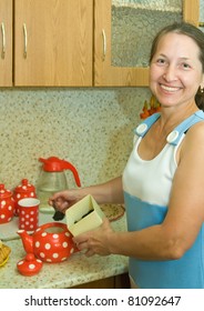 Elderly Woman Making Tea  In Red Teapot At Kitchen