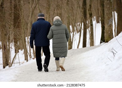 Elderly Woman And Man Walking In Winter Park, Rear View. Old Couple In Warm Clothes During Snow Weather, Concept Of Old Age