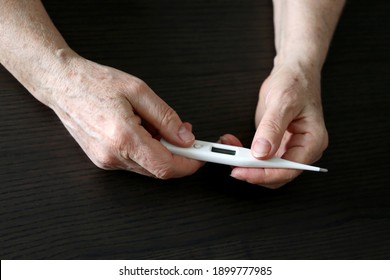 Elderly Woman Measuring Body Temperature, Concept Of Fever, Coronavirus Symptoms. Digital Thermometer In Wrinkled Female Hands Close Up