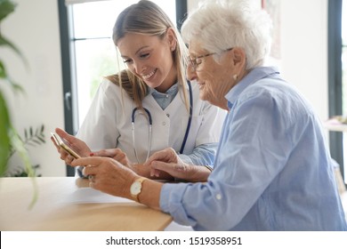 Elderly woman with nurse at home looking at tablet
