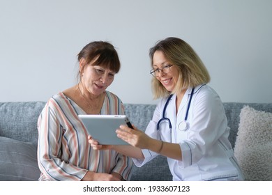 Elderly Woman With Nurse At Home Looking At Tablet. Doctor Holding In Hand Digital Tablet And Giving Advice To Her Patient. Elderly People Healthcare Tech Concept.
