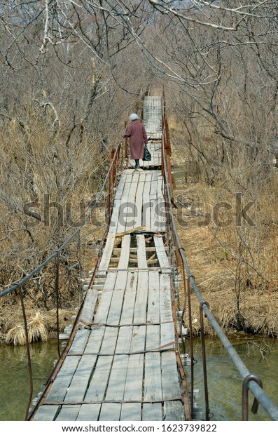 The elderly woman on hanging footbridge across a\
small river.