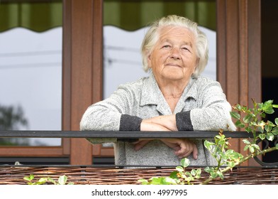 Elderly Woman On The Porch Of Her House.