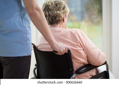 Elderly woman on wheelchair is looking through the window - Powered by Shutterstock