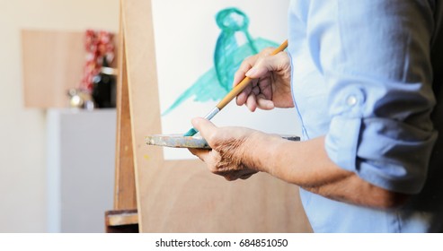 Elderly woman painting for hobby. Active senior person at art school. Closeup of old female hand with brush and palette, mixing color paints - Powered by Shutterstock