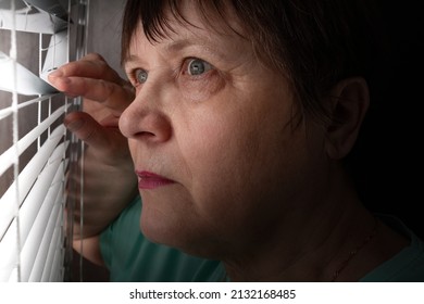 An Elderly Woman Peers Through The Blinds Through The Window.