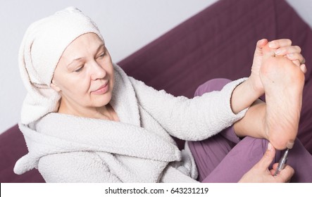 Elderly woman performing pedicure with special devices at home