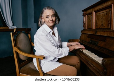 Elderly woman playing the piano sitting on a chair in a white shirt