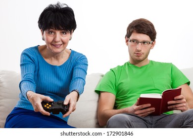 Elderly woman is playing video game while her son is reading a book