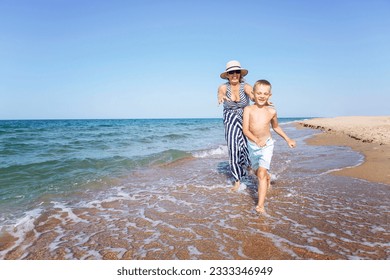 An elderly woman plays with a boy on the seashore. Laughing grandmother and grandson run along the sandy beach. Love and tenderness. Active lifestyle, health and relaxation at the resort.  - Powered by Shutterstock