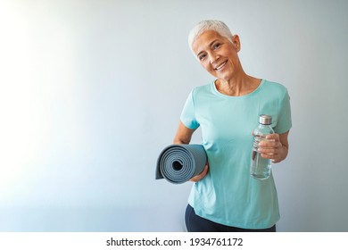 An elderly woman poses for a portrait after her workout. Fit Mature Woman With Exercise Mat. Confident Woman With Exercise Mat Smiling In Gym 