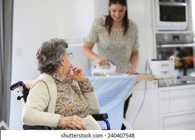 Elderly Woman Reading Book While Home Helper Irons Laundry