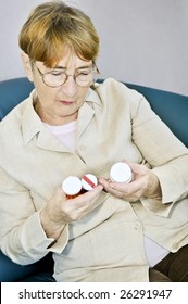 Elderly Woman Reading Warning Labels On Pill Bottles With Medication