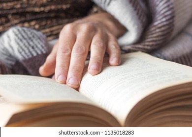 An elderly woman reads a book. The woman's hand lies on an open book. Reading the Bible and praying